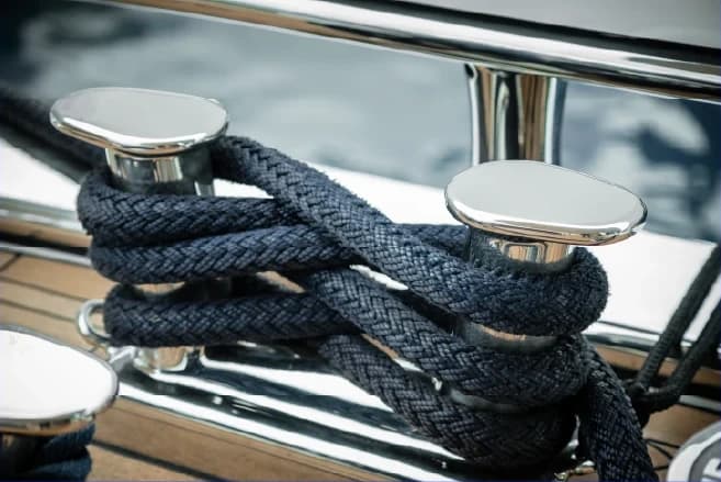 Navy mooring lines wrapped around polished stainless bollards on a teak deck