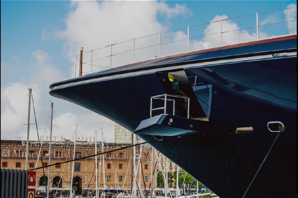 The dark blue bow of a superyacht towering over masts in a Mediterranean marina